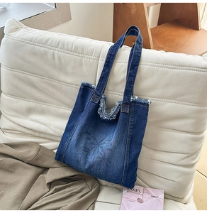 Detail of frayed edges and palm tree print on dark blue denim shoulder tote bag