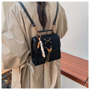 Detail of black leather backpack with gold butterfly charm and beaded tassel detail
