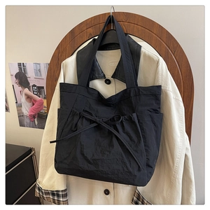 Detail of black canvas tote bag with bow tie decoration and wide shoulder strap