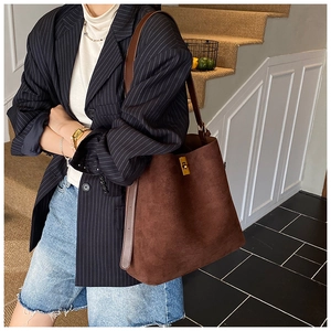Detail of dark brown suede tote bag featuring a gold metal buckle and leather strap