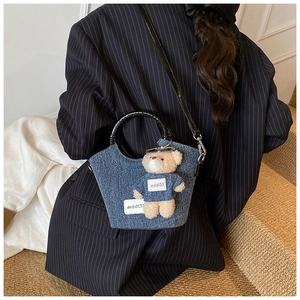 Detail view of denim bucket bag with plush bear charm and black patent leather handles