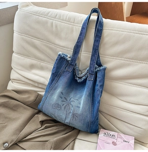 Detail of frayed edges and beach palm tree print on blue denim shoulder tote bag