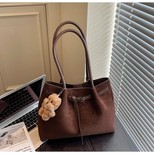 Detail of dark brown suede tote bag with plush bear charm and long leather handles
