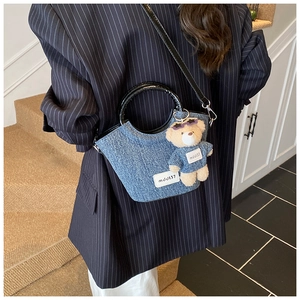 Detail of blue denim bucket bag with teddy bear charm and sleek black handle on model