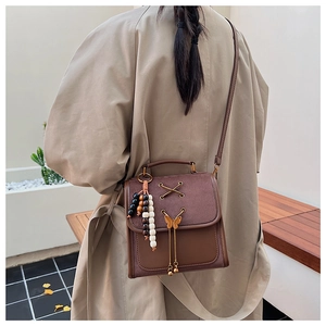 Detail of a brown leather crossbody bag featuring a metal butterfly and fringe tassels