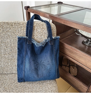 Detail of dark blue denim tote bag with frayed edges and tropical palm tree print design