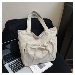 Detail of beige pleated tote bag with bow drawstring and side pockets on a chair