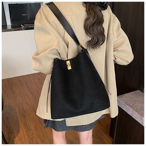 Detail of black suede tote bag with golden twist lock and leather strap shown on model