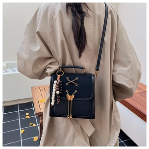 Close-up of black crossbody bag with golden bow hardware and wooden bead charm detail