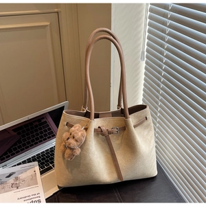 Detail of beige suede tote bag featuring brown strap accents and a plush bear charm