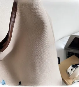 Close-up of beige canvas tote bag material with brown leather piping and brand tag