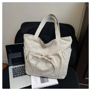 Detail of off-white pleated canvas tote bag featuring a decorative drawstring bow and front pocket