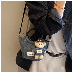 Borsa a secchiello in denim blu con manici rotondi e ciondolo a orsetto su una modella