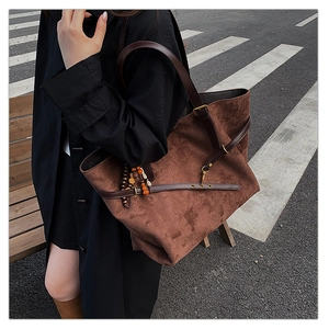 Detail of coffee brown suede tote bag with leather strap and wooden bead charm on a city street