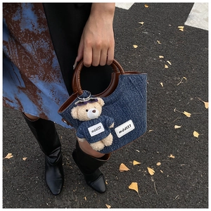 Dettaglio della borsa a secchiello in denim blu con manici marroni e ciondolo a forma di orso