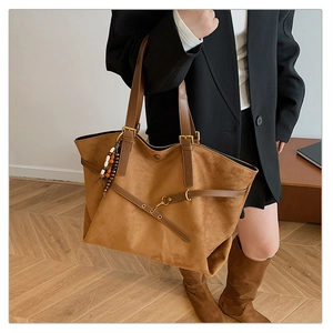 Detailed view of brown suede tote bag with leather strap and decorative wood bead charm
