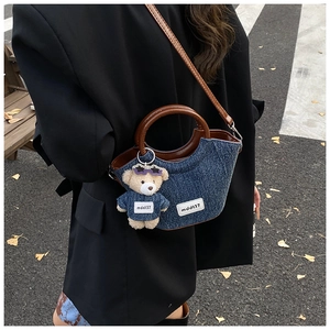 Detail shot of denim bucket bag with leather handles and cute bear charm accessory