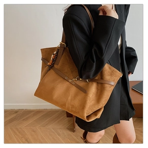 Detail view of large brown suede tote bag with leather straps and beaded charm decoration