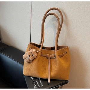 Detail of camel tote bag with buckle strap and cute plush bear charm on a chair