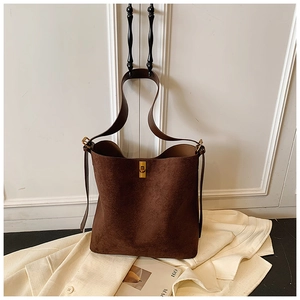 Detail of dark brown suede bucket bag with gold clasp and thick strap on suit jacket