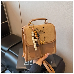 Detail of beige bow backpack with gold buckle and wooden beads on a book