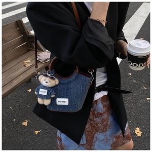 Close-up of denim bucket bag with brown leather strap and a cute bear keychain accessory