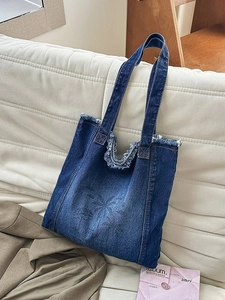 Deep blue denim tote bag with frayed edges and palm tree print on a leather sofa