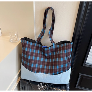 Grand sac cabas à carreaux bleu et marron posé sur une valise pour le voyage
