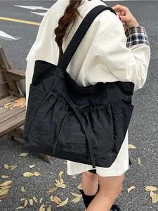 Large black canvas tote bag with bow detail and side pockets in an outdoor street setting