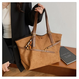 Detailed close-up of brown suede tote bag with leather handles and beaded tassel accessory