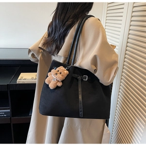 Detail of black suede tote bag with metal buckle strap and cute brown bear pendant