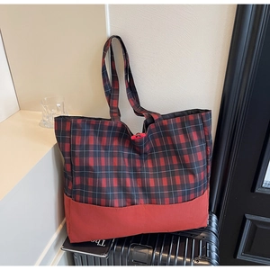 Gros plan d'un grand sac cabas à carreaux rouges posé sur une valise noire élégante