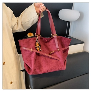 Detail of burgundy faux suede tote bag featuring a beaded tassel charm and leather straps