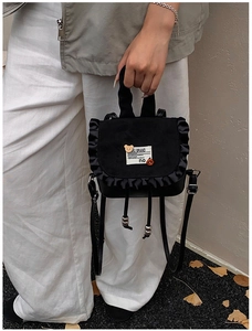Detail of mini black backpack with bear accent and elegant ruffle trim on the flap