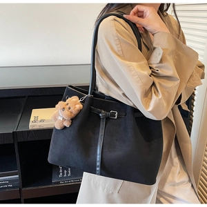 Detail of black suede tote bag with leather strap and plush puppy charm on trench coat