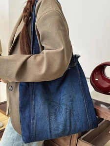 Deep blue denim tote bag with palm tree print and frayed edges worn by a model