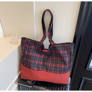 Détail du grand cabas à carreaux rouges et noirs avec anses larges sur une valise