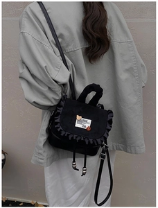 Detail of a black mini backpack featuring ruffled edges and decorative brand patches