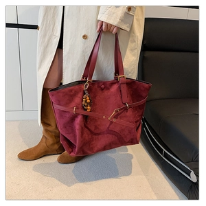 Detail of burgundy suede tote bag with metal buckles and colorful beaded pendant