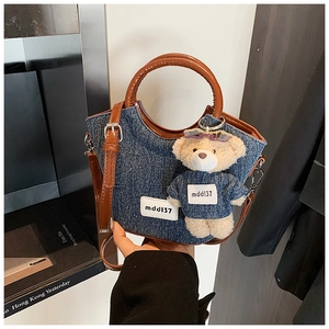 Dettaglio della mini borsa tote in denim con manici in pelle marrone e ciondolo a orso