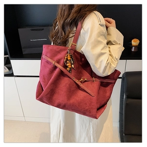 Macro view of burgundy suede tote bag featuring vintage wooden beads and metal buckle strap