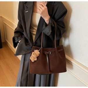 Detail of dark brown suede tote bag featuring slim straps and a cute plush bear charm