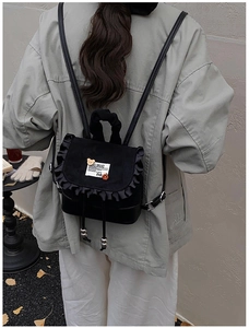 Close-up detail of black PU leather mini backpack with ruffle design and bear patch