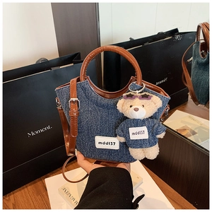 Dettaglio della borsa a secchiello in denim con manici in pelle marrone e orsetto