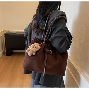 Detail of dark brown faux suede tote bag with plush bear charm in minimalist interior