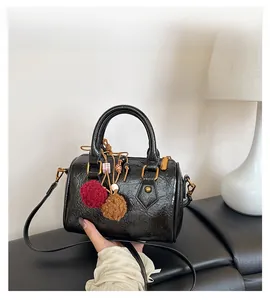 Detail of black glossy oil wax cylinder bag with gold hardware and colorful pompom