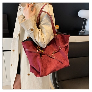 Detail of burgundy suede tote bag featuring wooden bead charm and matte leather texture