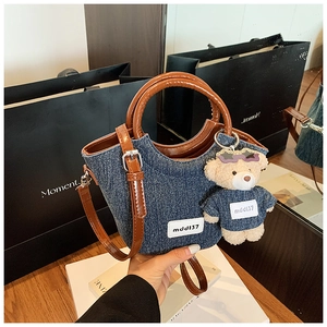 Dettaglio borsa a secchiello in denim con manici in pelle e ciondolo a forma di orsetto