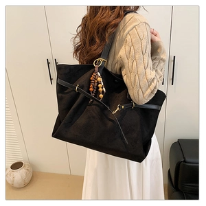 Macro view of black suede tote bag with retro beaded pendant and vintage metal buckle detail
