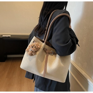 Detailed side view of a large beige suede tote bag with brown straps and bear charm